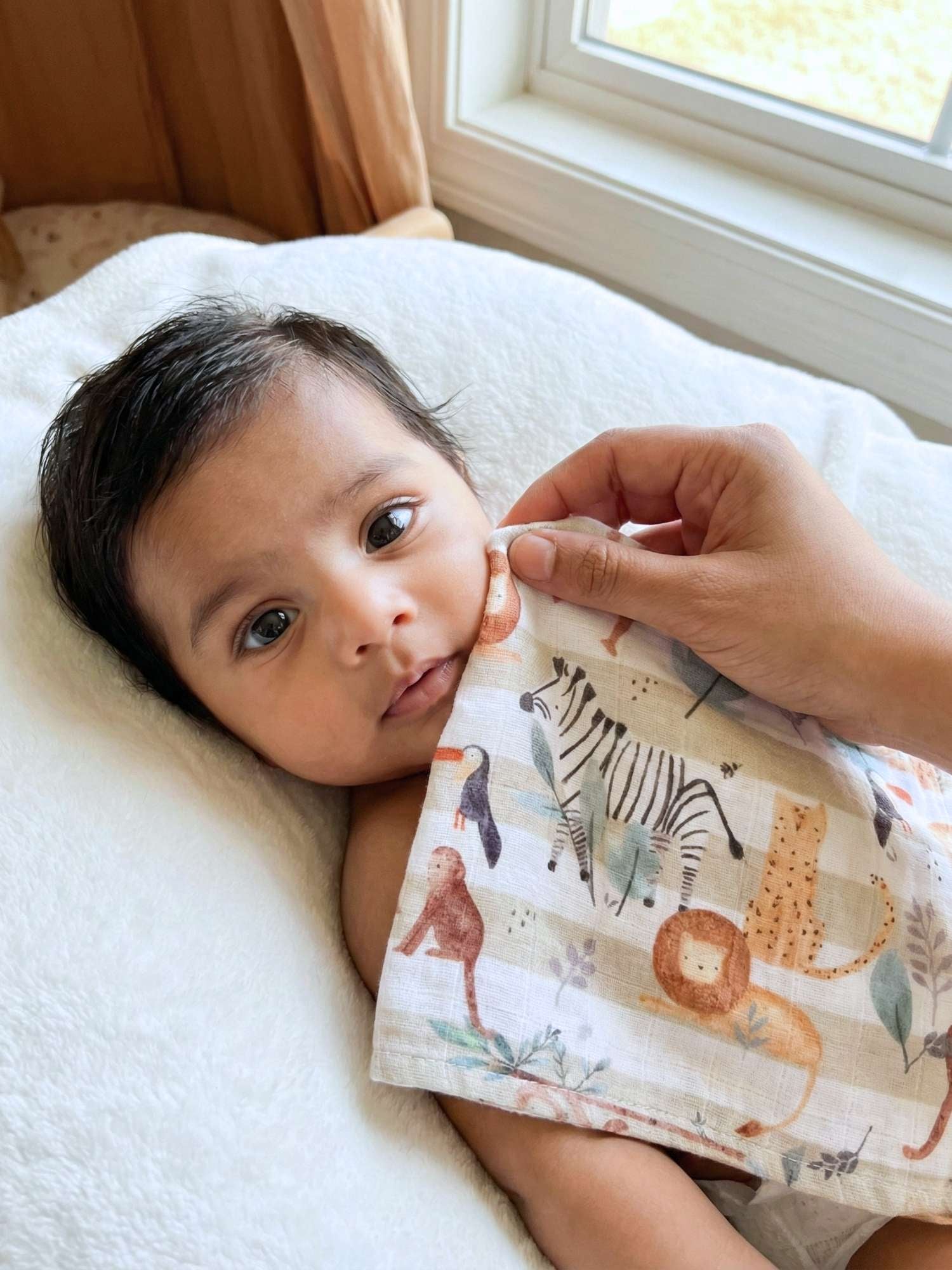 Baby being wiped with a soft bamboo muslin wash cloth featuring animal prints in a room with a window.